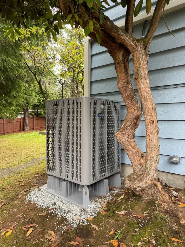 Outdoor heat pump unit installed on a gravel pad beside a Seattle area home.
