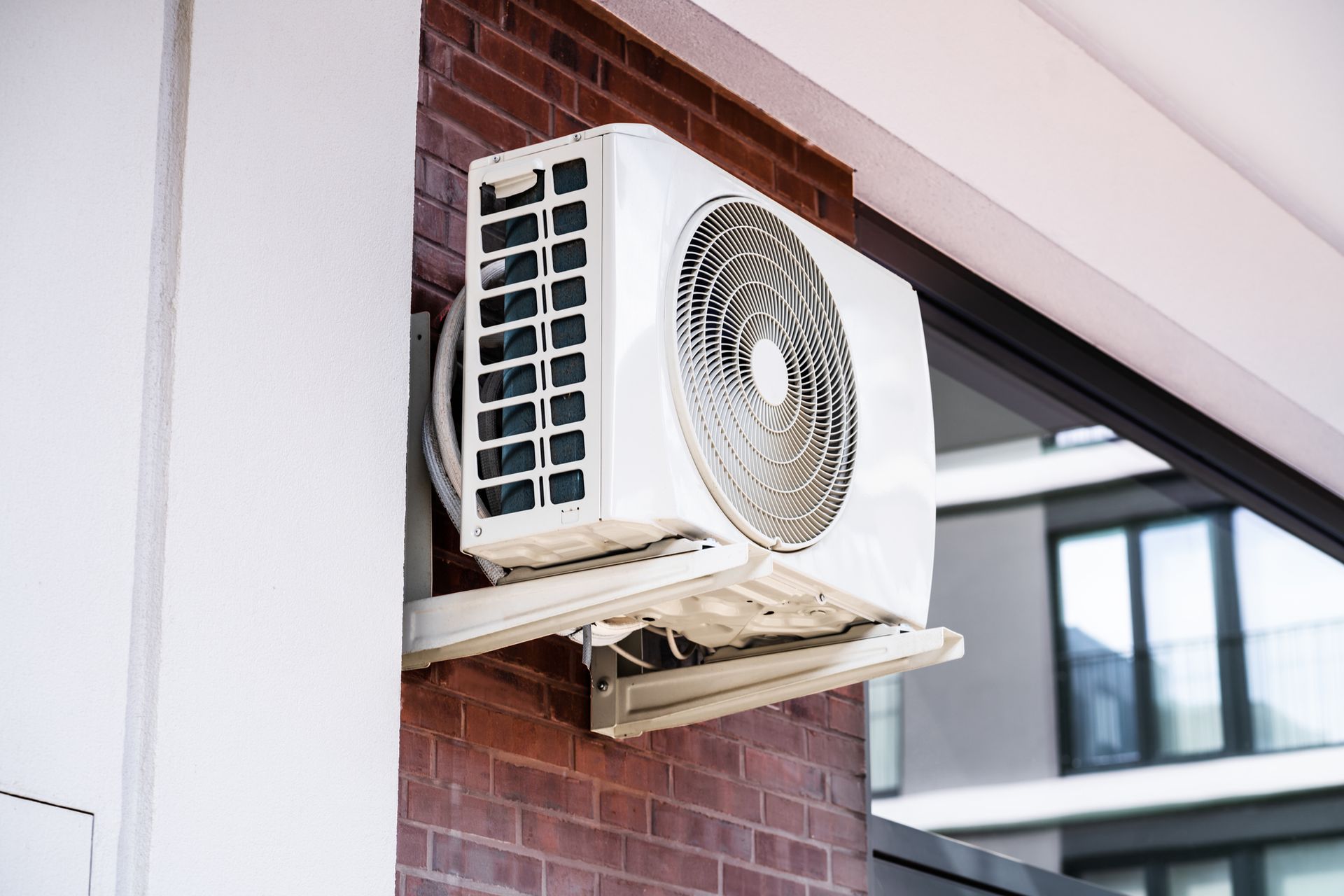 A white air conditioner is mounted on a brick wall.