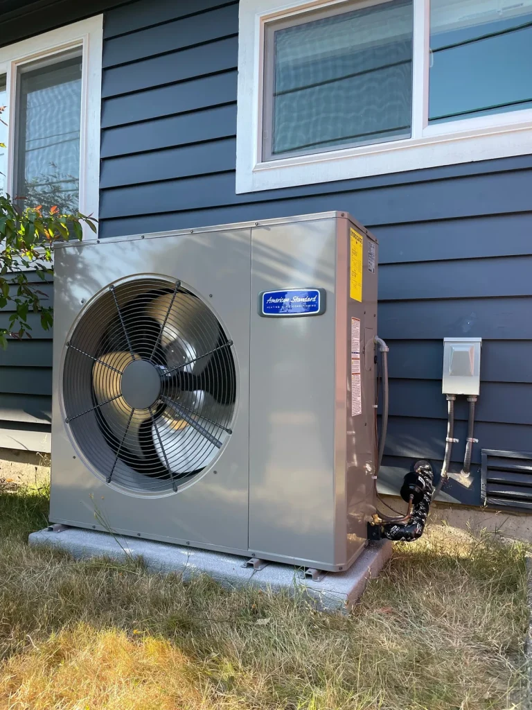 American Standard heat pump installed on a pad beside blue lap siding