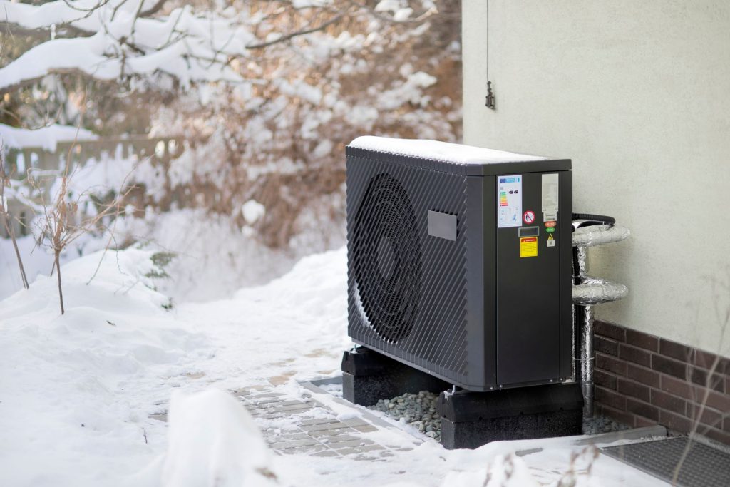 Seattle home in winter with heat pump outdoor unit being cleared of leaves and debris by technician.