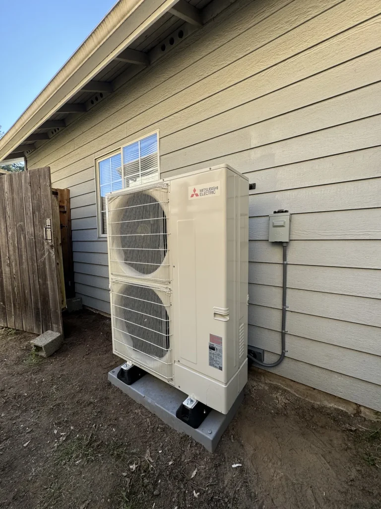 Mitsubishi dual-fan heat pump installed beside a wood fence
